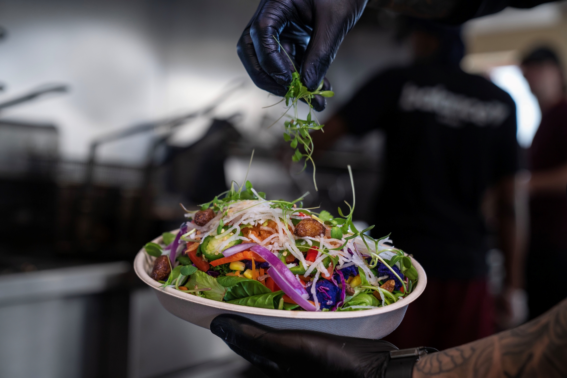 A chef garnishing a fresh salad bowl with microgreens at Balance Grille, featuring a colorful mix of vegetables like red onion, corn, and avocado.