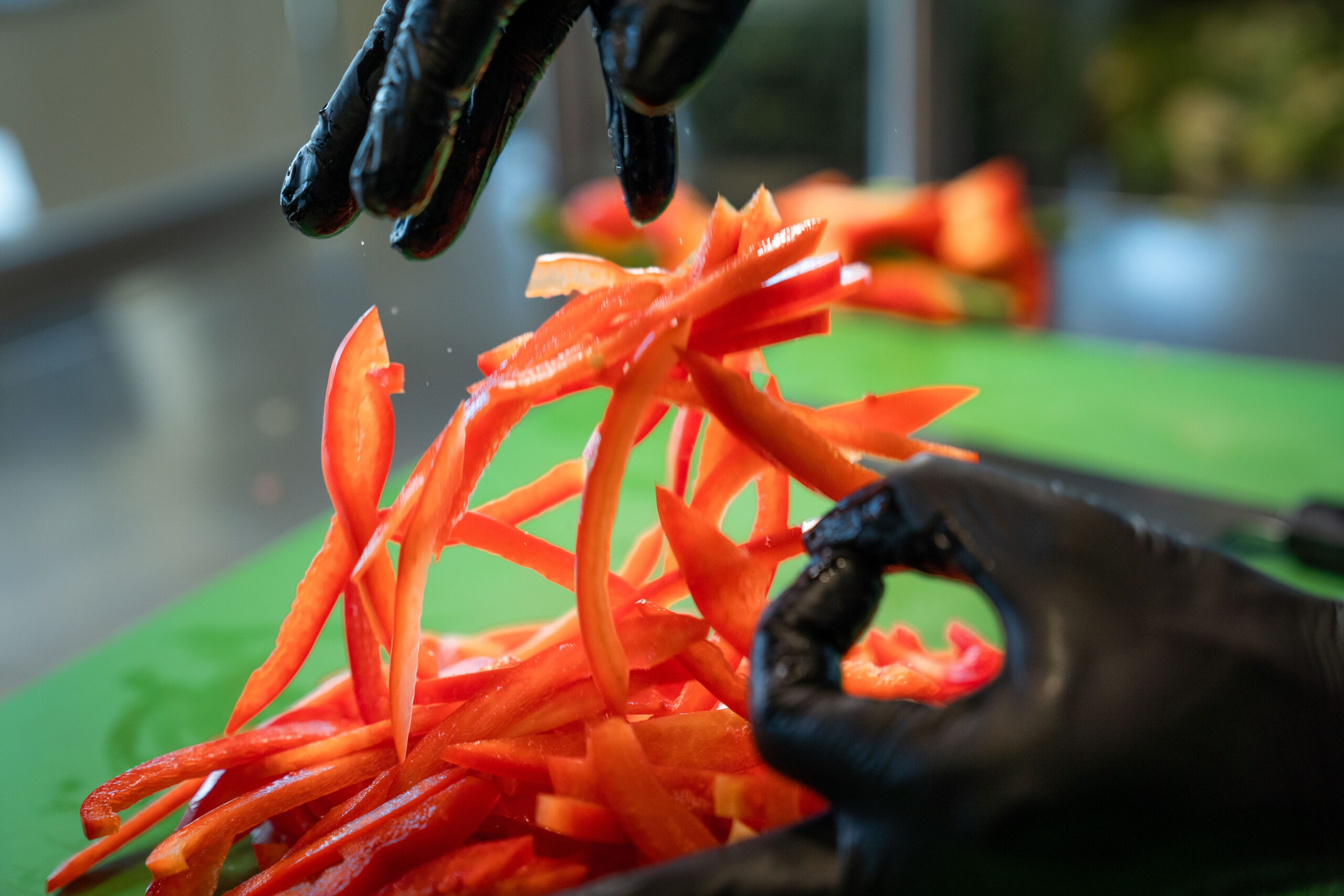 Chef CJ in black gloves tossing freshly sliced red bell peppers on green cutting board at Balance Grille.