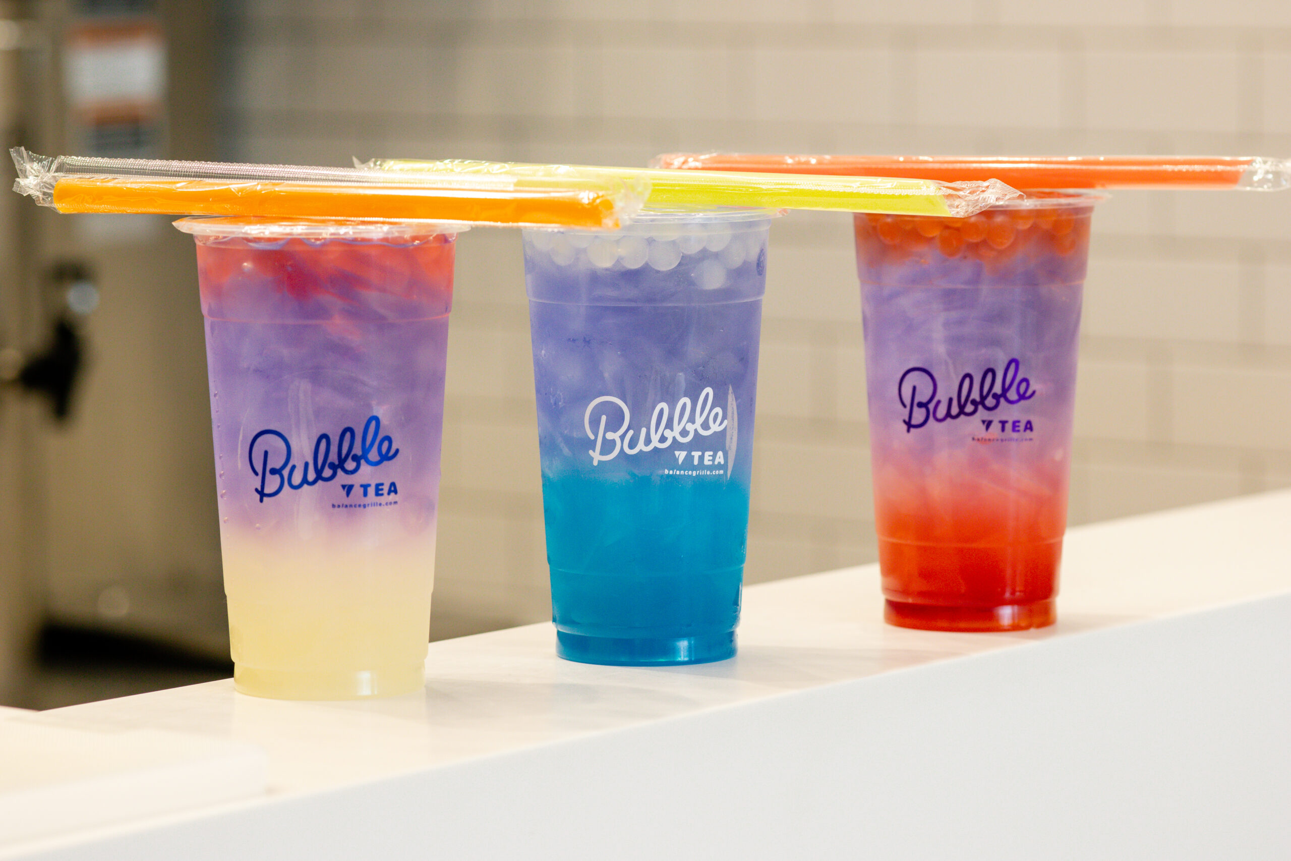 Three colorful gradient bubble teas topped with straws, served at Balance Grille with fruit bubbles and butterfly tea.