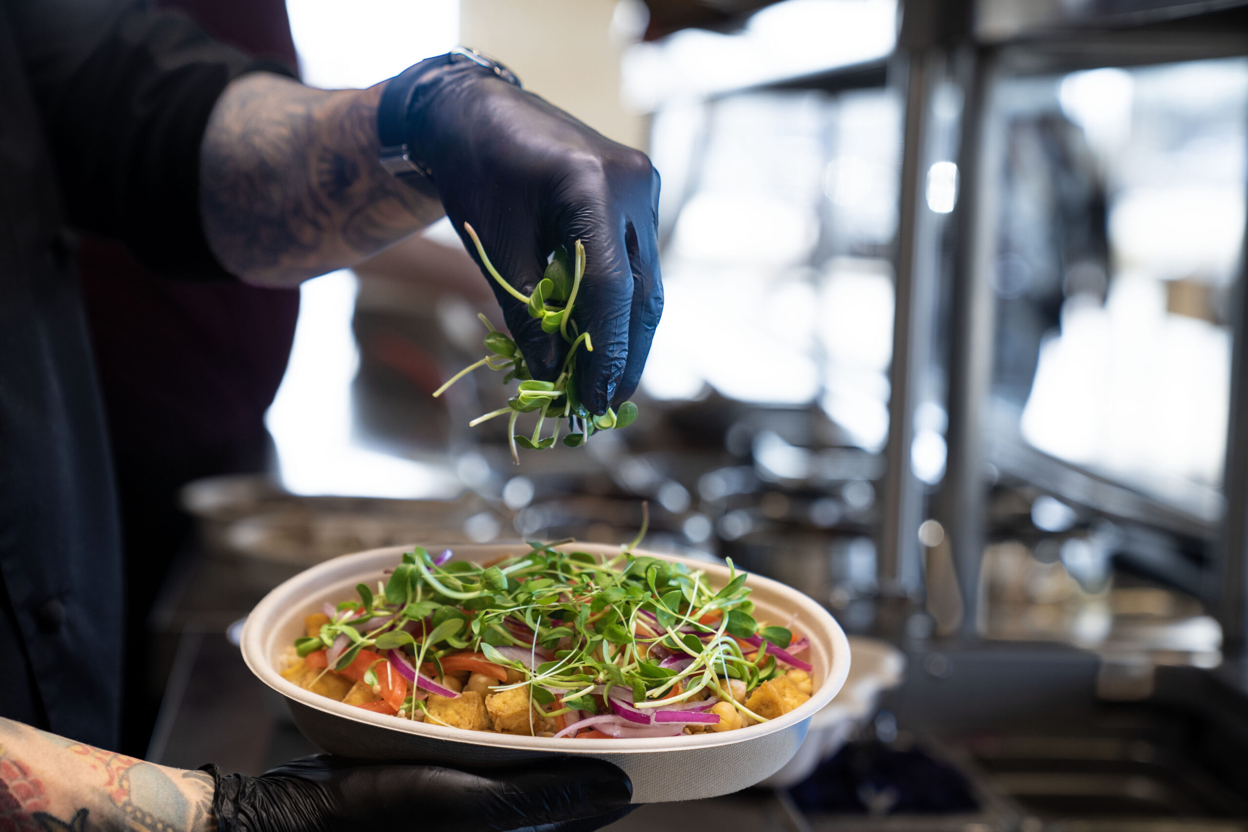 A Balance Grille team member garnishes a vibrant rice bowl with Balance Farms microgreens behind the counter in the kitchen.