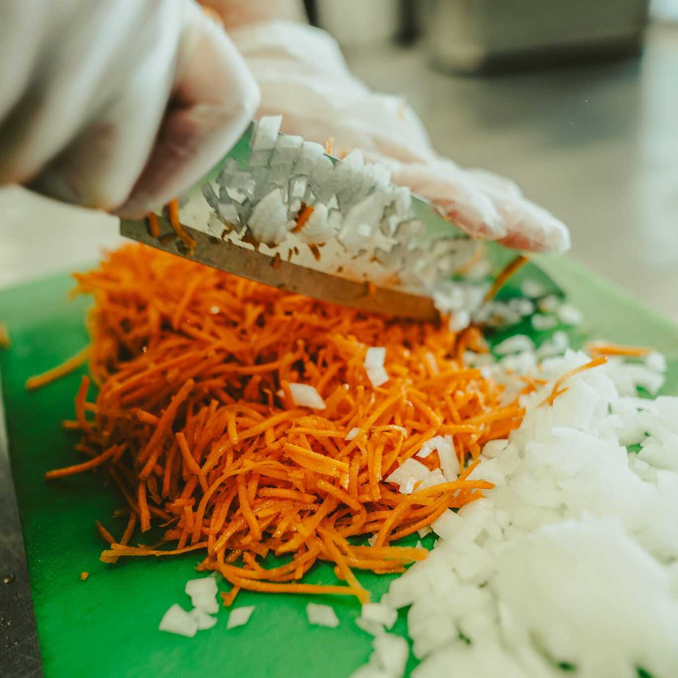 Gloved hand finely chopping white onions and shredded carrots at Balance Grille.