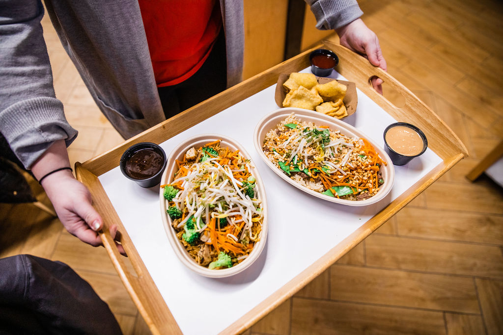 Two Asian rice bowls are placed on a wooden tray with three small bowls of sauce.