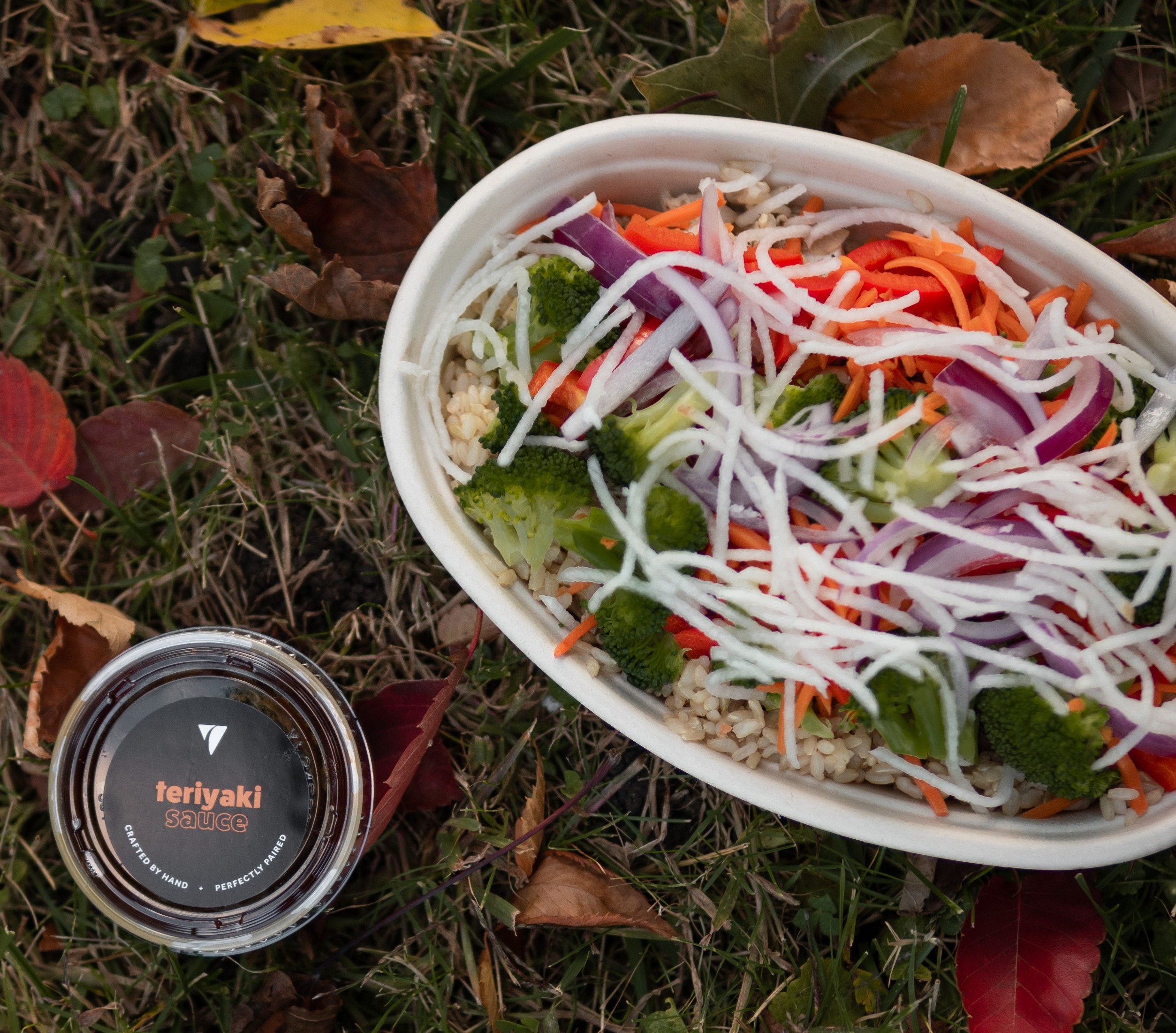 A Balance Grille rice bowl and teriyaki sauce placed on the ground side by side.
