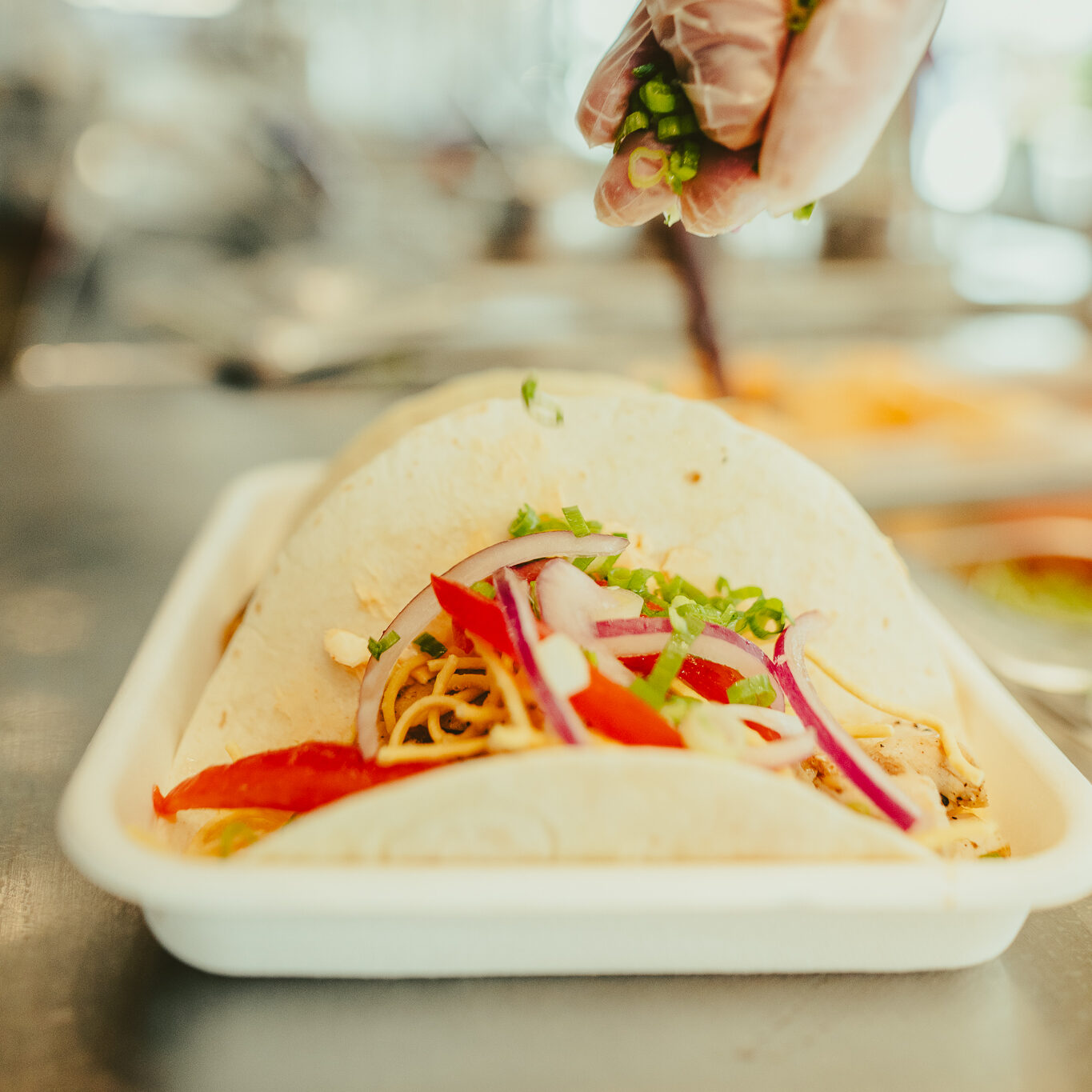 Chef’s hand sprinkling fresh toppings onto a taco at Balance Grille.