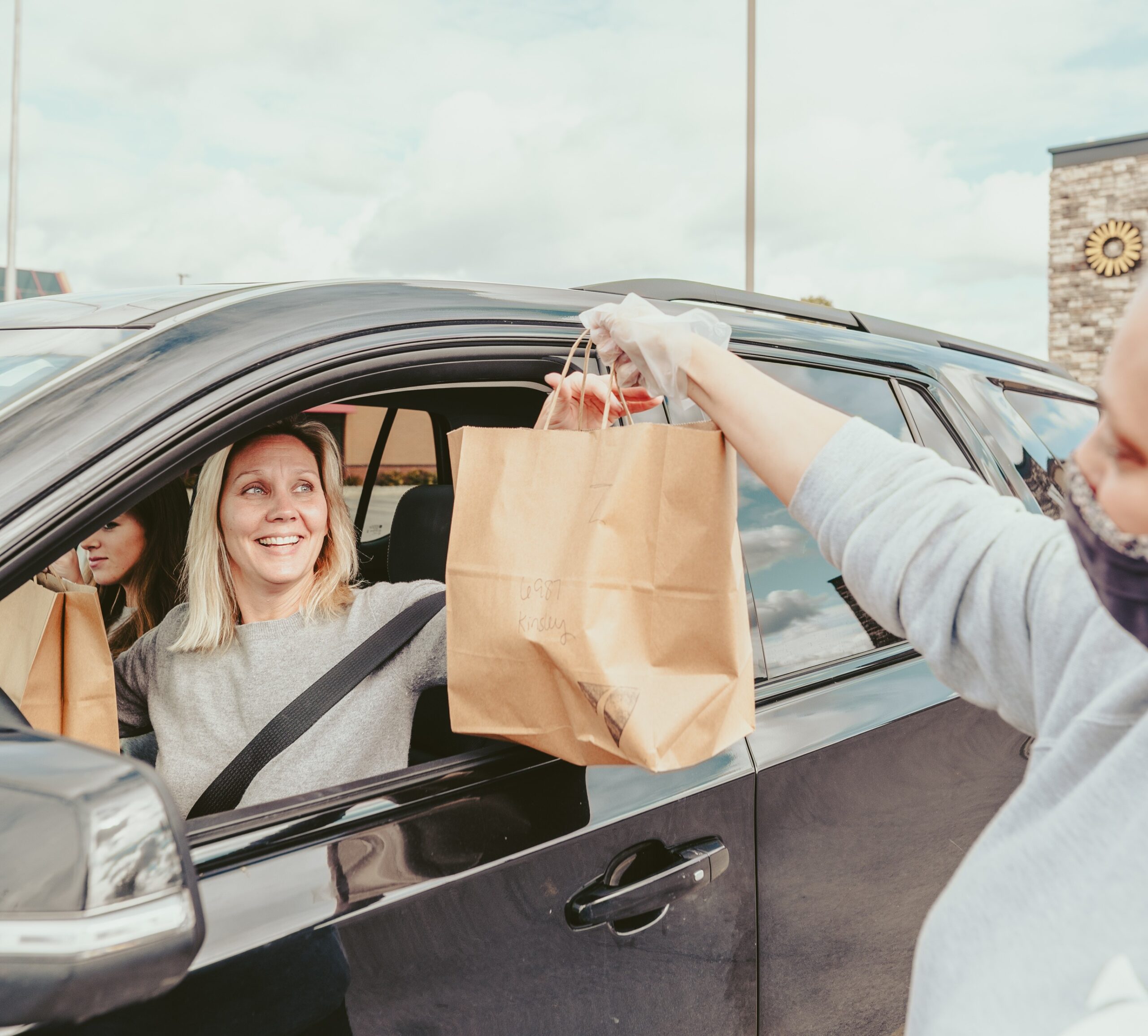 An employee from Balance Grille is handing over Hot & Sour Soup in a brown bag to a customer.