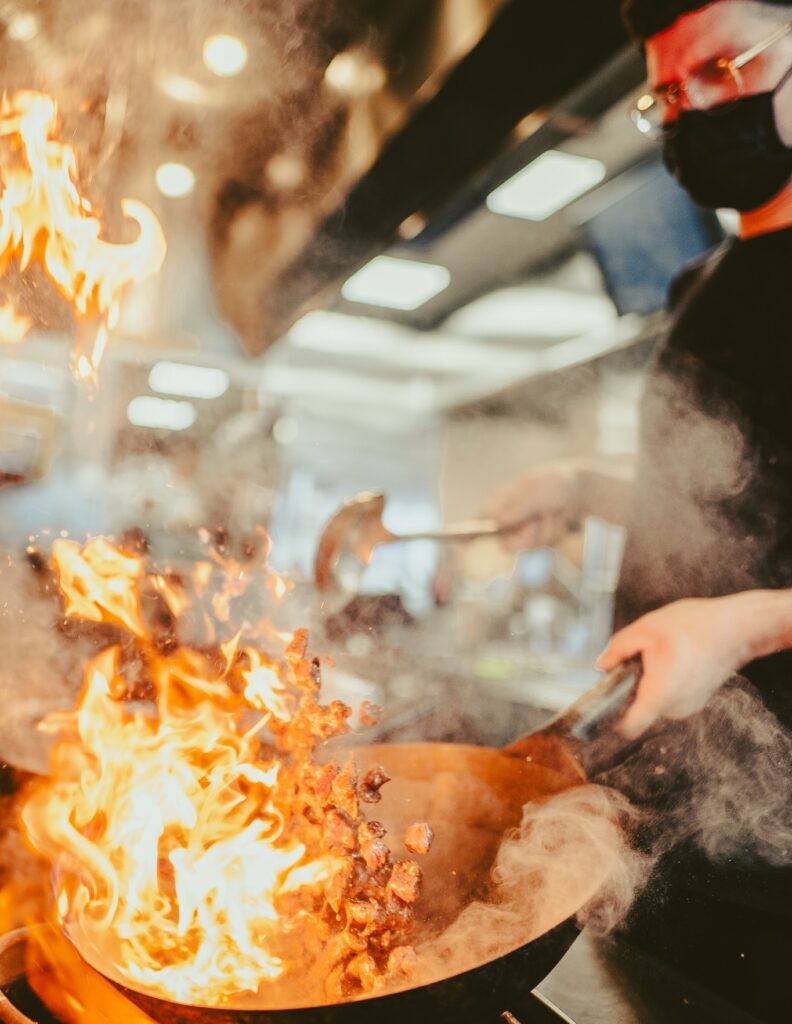 A chef cooking steak in a wok inside Balance Grille.